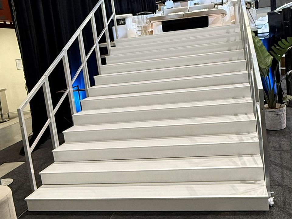 White steps with a handrail leading up to a display stage, with black drapes behind