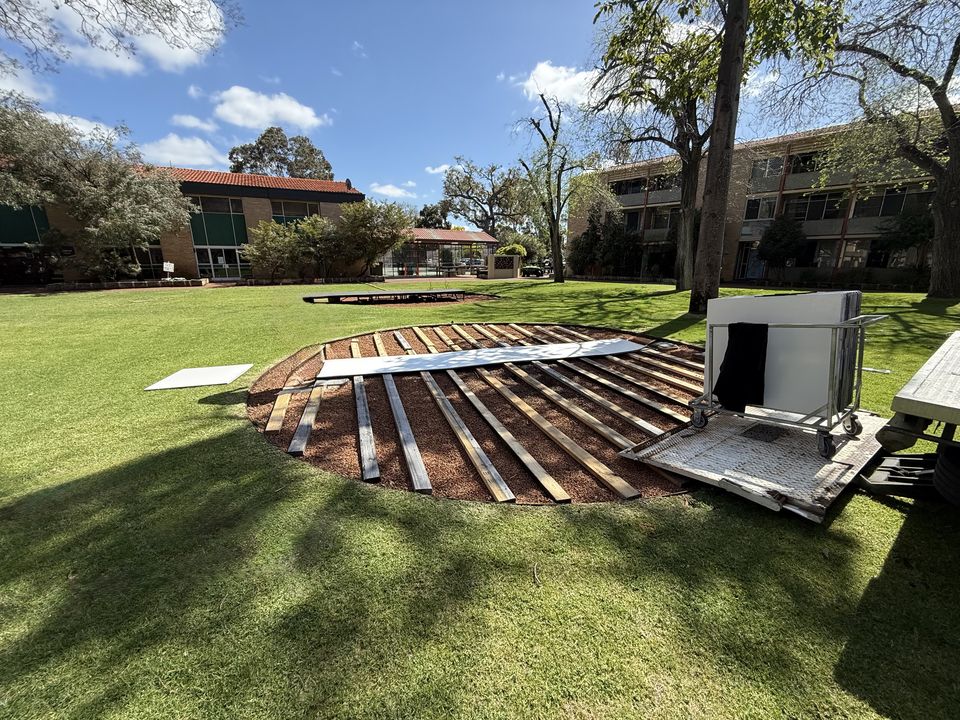 Timber frame being built over a fire pit on a lawn, ready for the dance floor