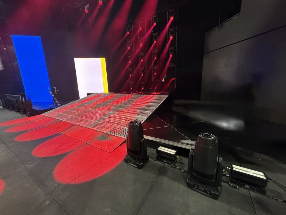 Silver mesh stage deck with angled edges under red concert lighting