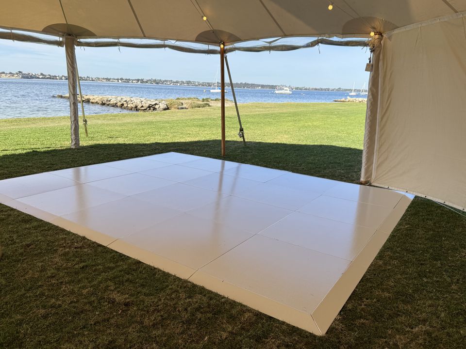 White dance floor on grass inside a sailcloth tent, with the river and moored boats behind