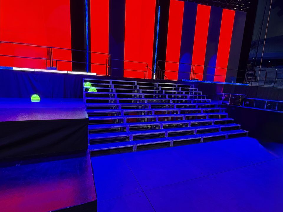 Wide stage stairs lit blue in front of red LED walls on a concert set