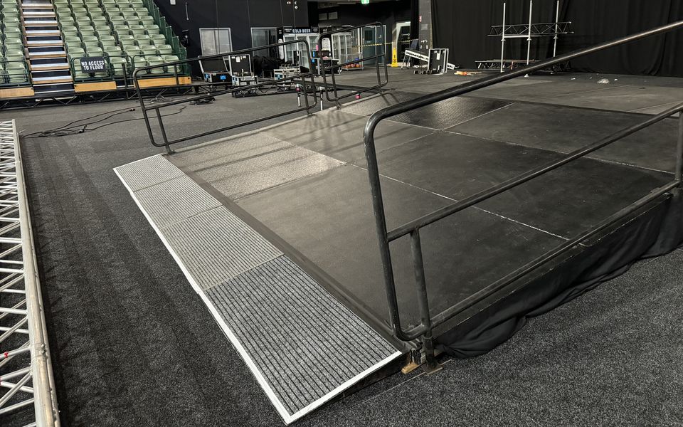 Access ramp with handrails leading onto a black stage in an indoor arena