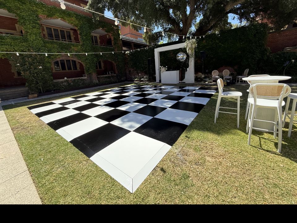 Black and White Check dance floor on a courtyard lawn, with festoon lights strung overhead and an ivy-covered brick building behind