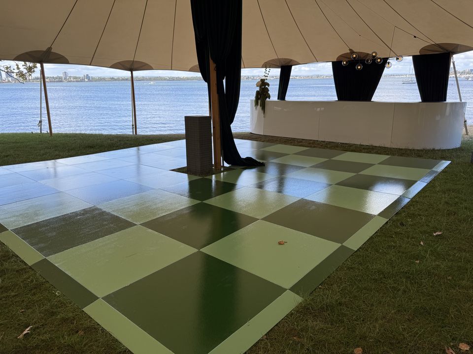 Green chequered dance floor on grass under a sailcloth tent beside the river
