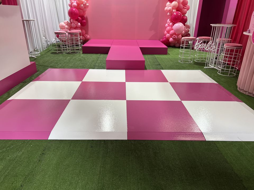 Pink and white checkered dance floor on turf in front of a pink stage with balloon garlands